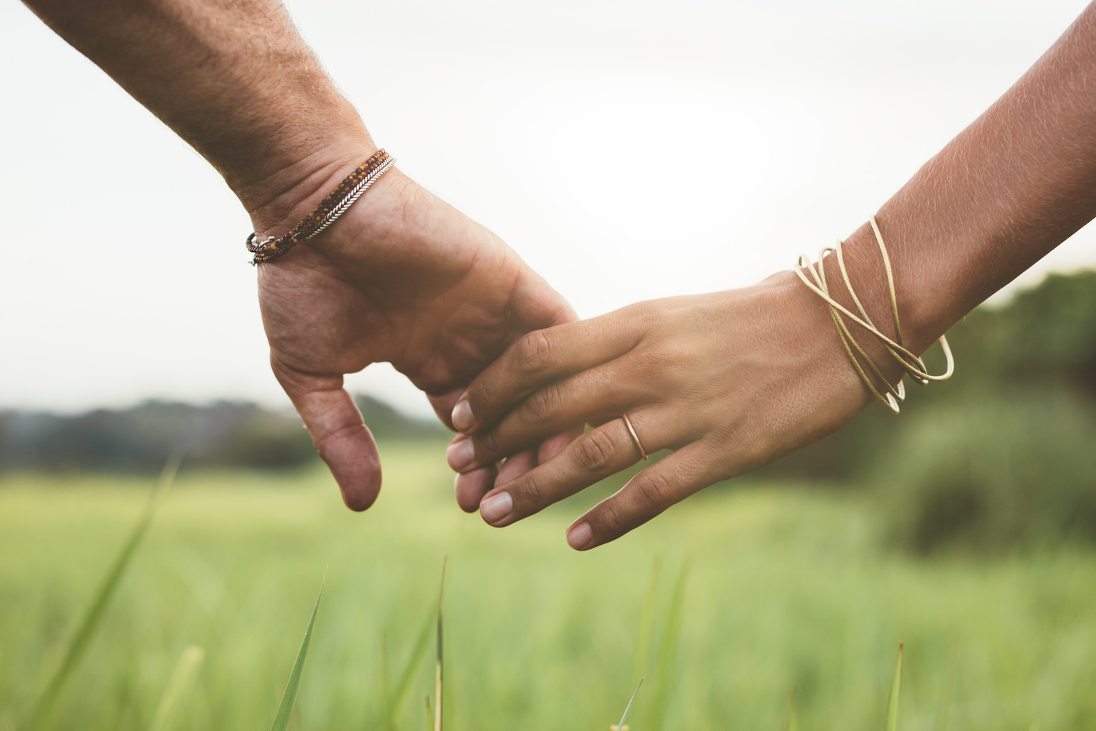 Horizontal shot of young couple walking through meadow holding hands with focus on hands .