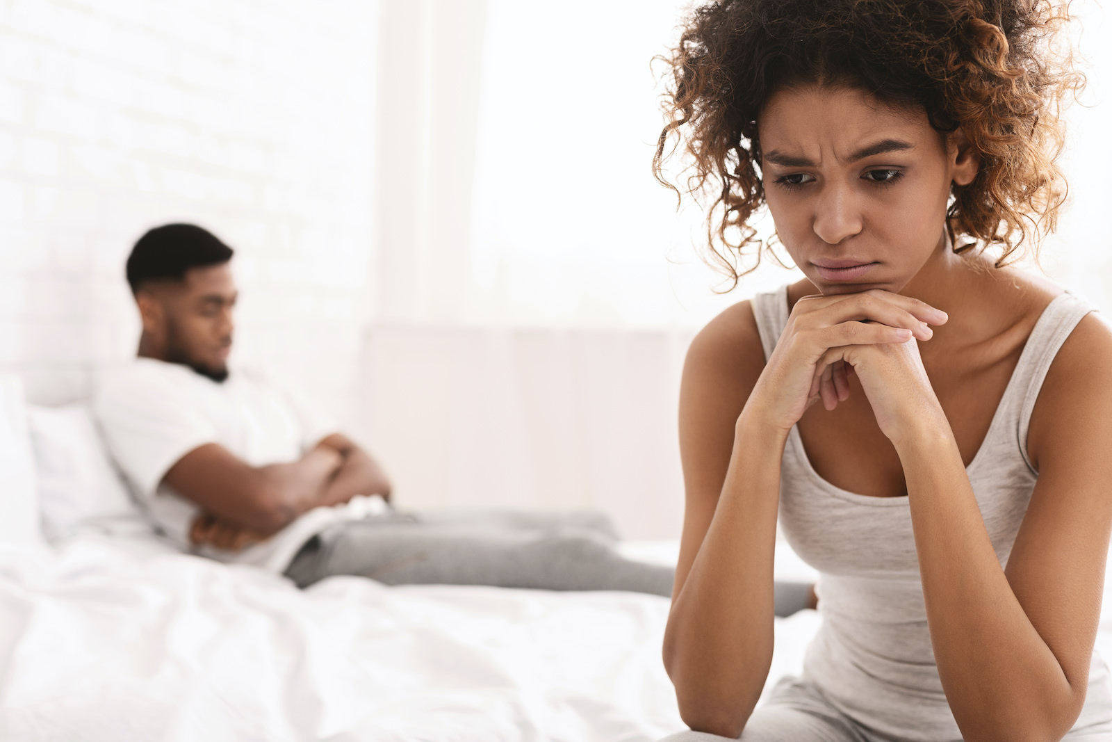 Thoughtful couple after quarrel lost in thoughts. Frustrated black girlfriend sitting on bed, thinking about relationship problems, empty space